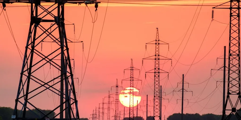 Electric transmission towers silhouetted against an orange sunset