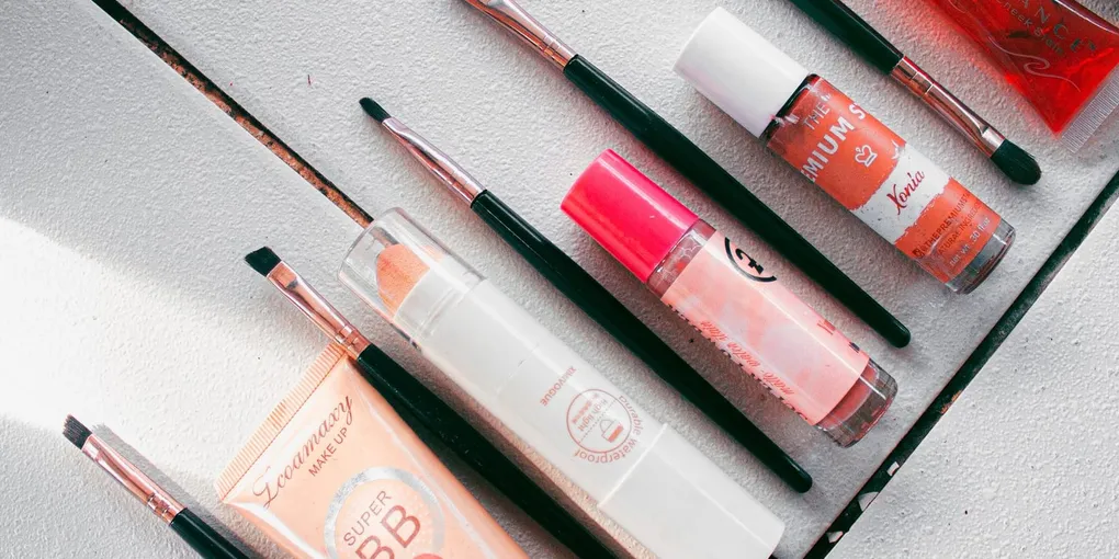 Flatlay of makeup products and brushes — BB cream, lip tints and a cheek stain — arranged on a white surface.