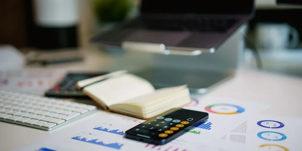 A laptop, calculator and printed financial charts on a desk