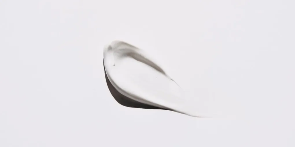 Close-up of a thick white moisturizer cream swirl on a plain background